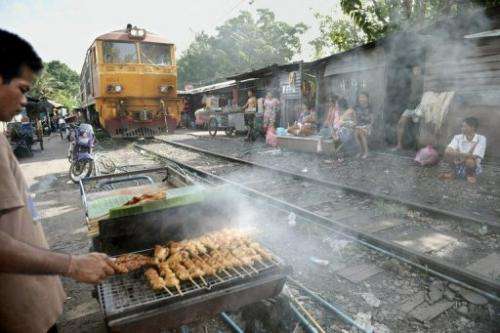 A man cooks barbecue chicken as a train passes by shack houses in Bangkok on October 28, 2008
