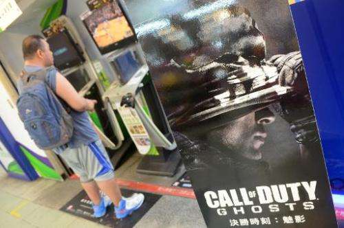 A man plays video games next to a sign advertising the videogame &quot;Call of Duty&quot; in Taipei on November 5, 2013