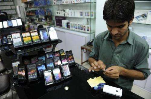 An employee pastes a screen protector onto a mobile phone at a shop in Islamabad on August 6, 2013