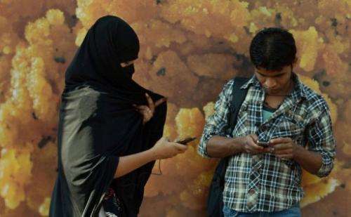 An Indian woman checks her mobile as she walks past a bystander in Mumbai, on February 20, 2013