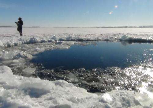 A police officer stands near a six-metre hole in the ice of a frozen lake, reportedly the site of a meteor fall, outside the tow