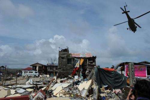 A rescue helicopter flies past a tattered national flag (C) and destroyed houses in the town of Hernani in Eastern Samar provinc