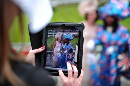 A woman at Ascot race course on June 20, 2013, photographs two other racegoers on a tablet computer
