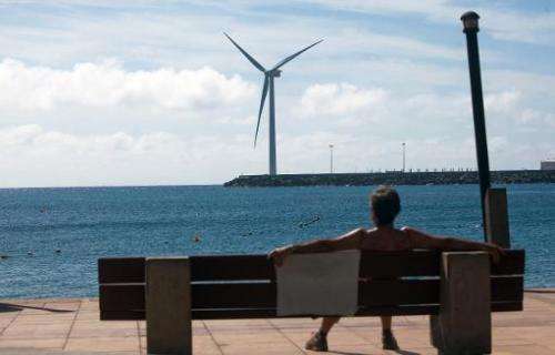 A woman sits on a bench backdropped by Spain's largest wind turbine. in the port of Arinaga, on Gran Canaria in the Spanish arch