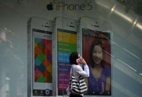 A woman uses a mobile phone as she walks past an Apple iPhone 5 poster outside a store in Beijing on September 11, 2013