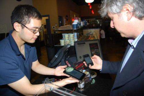 Customer David Lowy (right) uses his smart phone to pay .0101 bitcoins for a cup of dark coffee (worth about $2 US), from barist