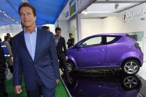 Former Governor of California Arnold Schwarzenegger walks past a Belumbery electric car in Geneva on March 8, 2012