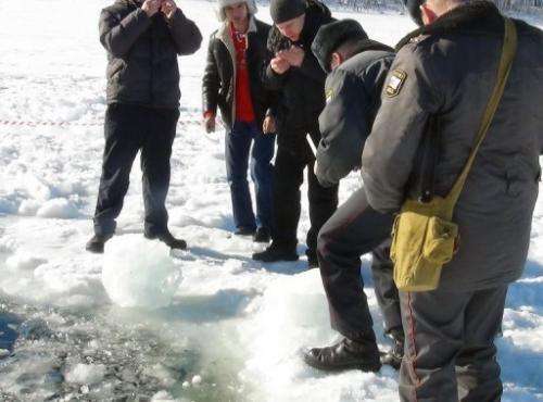 Officers are pictured on February 15, 2013 examining small objects near a hole in a frozen lake outside Chebakul