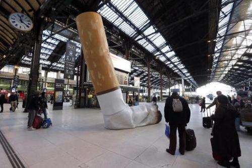 People pass by a giant mock-up discarded cigarette displayed on the ground at the Gare de Lyon railway station in Paris, on Dece