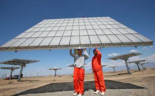 Workers check a solar panel in a field in Hami, China's Xinjiang region, on August 6, 2012