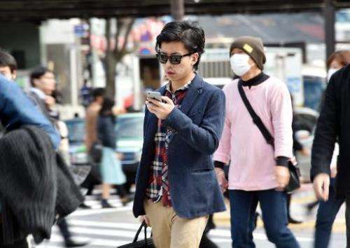 A pedestrian using his smartphone on a street in Tokyo, November 3, 2014. Growing ranks of cellphone addicts are turning cities 