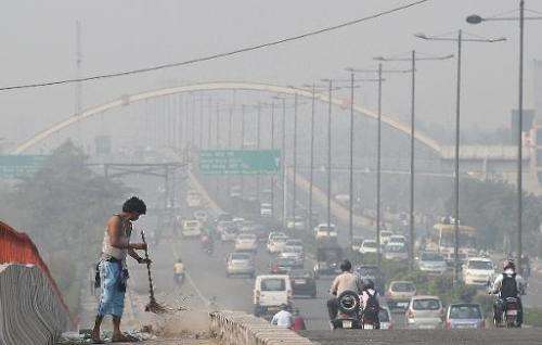 A sweeper cleans a flyover as smog covers the capital's skyline in New Delhi on October 24, 2014