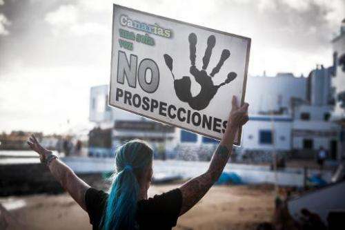 A woman holds a placard reading &quot;Canaries, only one voice: No prospections&quot; as she invites tourists to take part in th