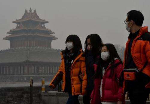 Chinese tourists wear face masks while walking past the Forbidden City as heavy air pollution shrouds Beijing on February 26, 20