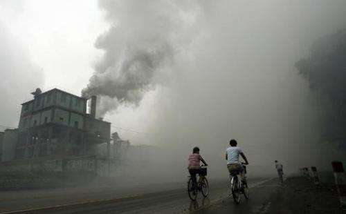 Cyclists pass through thick pollution from a factory in Yutian, China on July 18, 2006