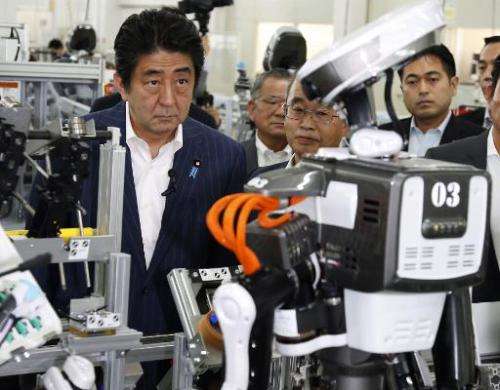 Japanese Prime Minister Shinzo Abe inspects a robot working at an assembly line of cash dispensers at a factory in Kazo, suburba