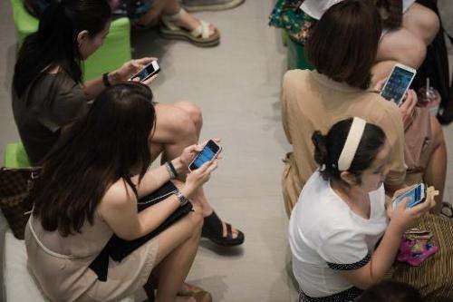 This picture taken on March 21, 2013 shows a group of people sitting down using their smartphones at a shopping mall in Bangkok