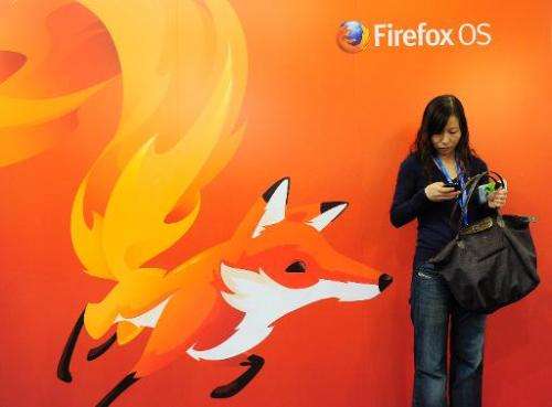A woman looks at her mobile phone as she stands in front of a poster of Mozilla Firefox onFebruary 27, 2013 at the Mobile World 