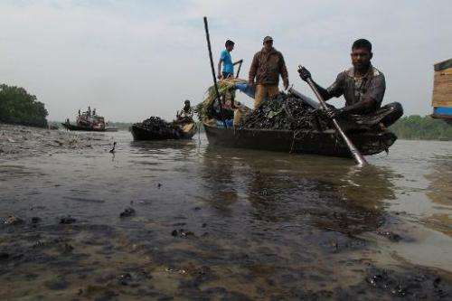 Bangladeshi villagers collect oil from their skiff in the Shela River in Mongla on December 13, 2014, after a ship carrying 350,