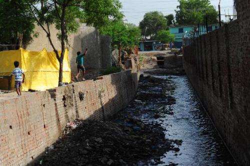 Children play by a polluted canal that runs into the river Ganges in the Jajmau area of Kanpur on June 26, 2014
