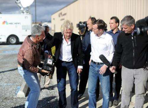 Virgin founder Sir Richard Branson(2ndL) helps a reporter (L) with his camera after the reporter fell to the ground after a pres