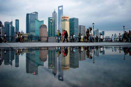 Pedestrians walk past the skyline of the city's financial district in Shanghai on October 8, 2010