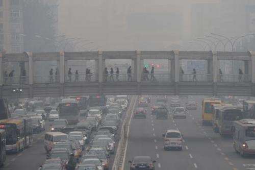 Pedestrians walk through an overpass as commuters drive on a road below in Beijing amid heavy smog on October 8, 2014