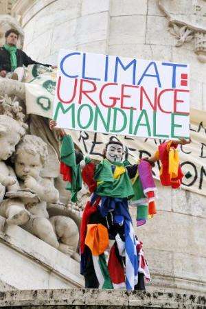 A climate protester wearing a Guy Fawkes mask holds a banner redaing &quot; World leaders act!&quot; on the Republique's statue 