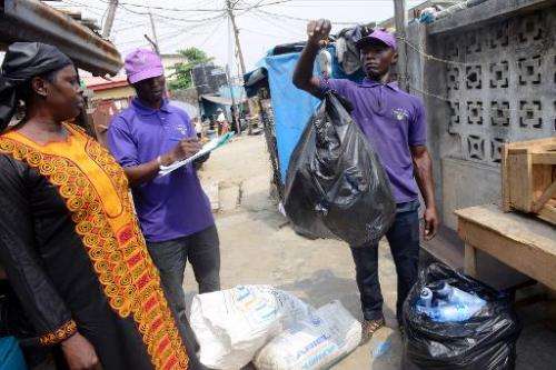 A customer (L) watches as staff of 'Wecycler' weigh and record recyclable goods, collected from her in Surulere district of Lago