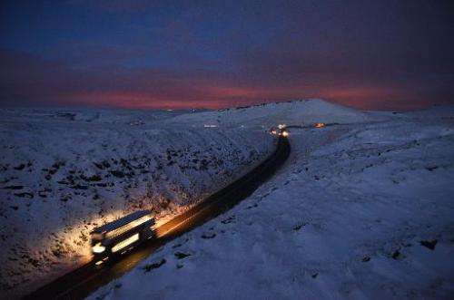 A double-decker bus travels over Standedge between snow-covered fields at dusk near the village of Diggle, northern England, on 