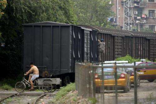 A man rides a tricycle over the rails next to a cargo train in Beijing on August 7, 2009