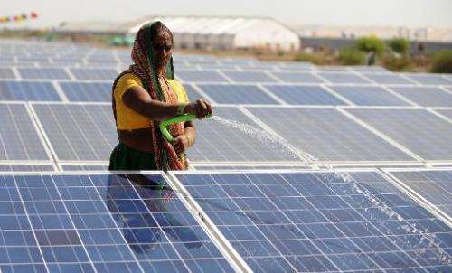 An Indian worker sprays water onto panels of India's first 1MW canal-top solar power plant at Chandrasan village of Mehsana dist