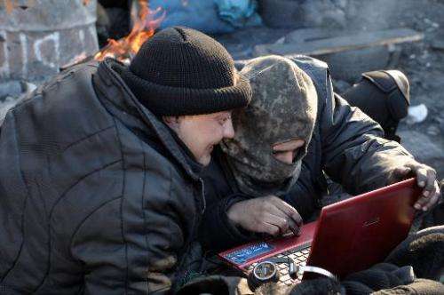 Anti-government protesters read the latest news via the internet on a laptop at a barricade in Kiev on February 5, 2014