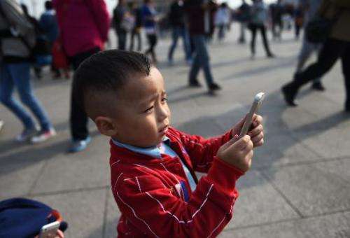 A young boy uses an iPhone to take photos in Tiananmen Square in Beijing on September 30, 2014. Apple began selling its latest i