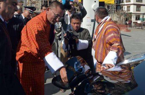 Bhutanese Prime Minister Tshering Tobgay (2nd L), watched by Nissan Motor CEO Carlos Ghosn (L), plugs in a receptacle to charge 