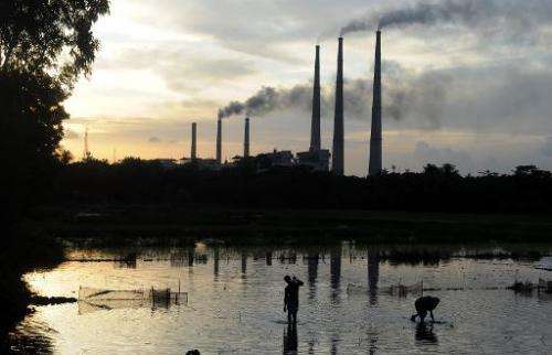 Farmworkers prepare a flooded field for rice-growing as the chimneys of the Kolaghat Thermal Power Plant loom the background in 