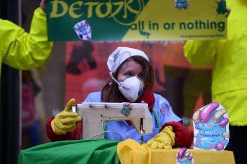 Greenpeace activists pretend they are sewing contaminated clothes with chemicals represented by little monsters, during a protes