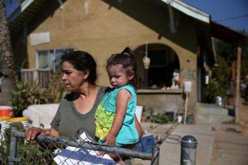 Jane Tapia (L) holds 1-year-old Melody in front of their home as they wait for a delivery of drinking water, in Porterville, Cal