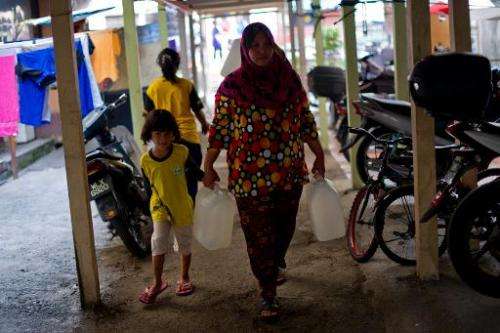 Norlizan, 40, (R), walks as she carries water containers in Balakong, outside Kuala Lumpur on February 25, 2014