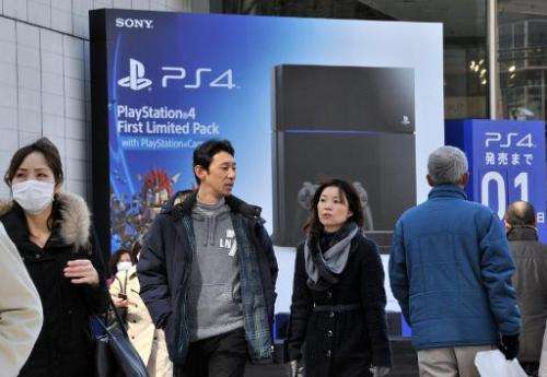 People pass before a large advertisement board of Sony Computer Entertainment's PlayStation 4 video game console at Tokyo's shop