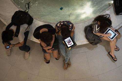 People use their smartphones and tablets in a shopping mall in Bangkok on March 19, 2013