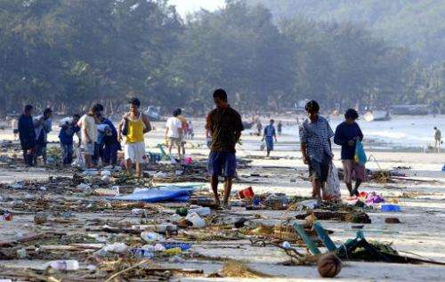 People walk through debris on Pathong beach on Phuket island, southern Thailand, on December 27, 2004, a day after a tidal wave 