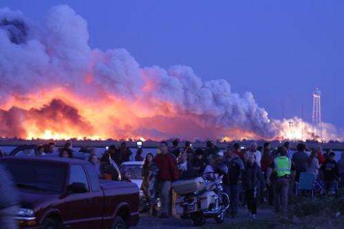 People who came to watch the launch walk away after an unmanned rocket owned by Orbital Sciences Corporation exploded (backgroun