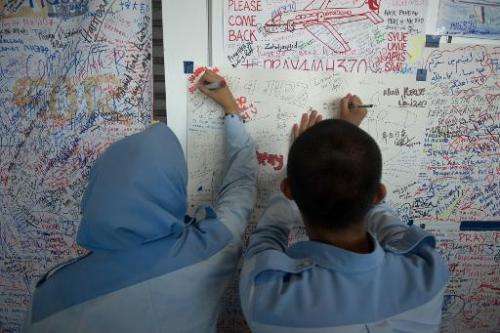 Students write on a placard carrying messages for the passengers of missing Malaysia Airlines flight MH370 at Kuala Lumpur Inter