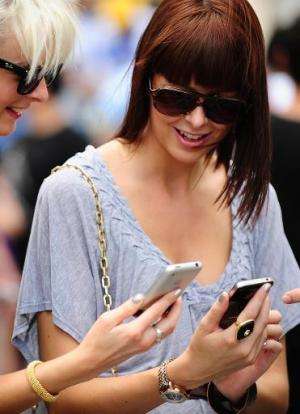 Two women look at smartphones in front of Manhattan's 5th Avenue Apple store on June 24, 2010 in New York