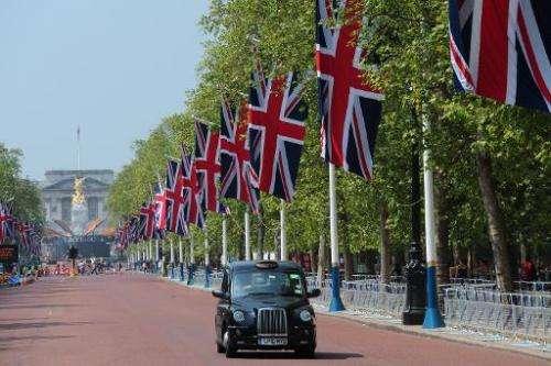Union Flags fly along The Mall as a taxi passes near the Queen Victoria Memorial statue and Buckingham Palace in London, on May 