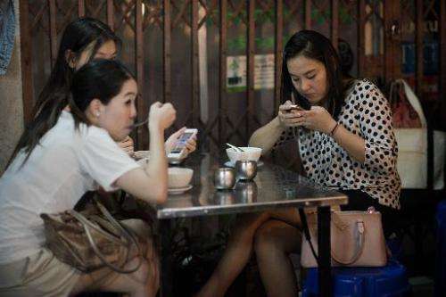 Women look at their smartphones while having dinner at a street food restaurant in Bangkok on March 19, 2013