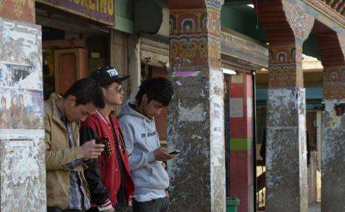 Young Bhutanese residents use mobile phones to surf the Internet as they stand on a street in Thimphu, February 20, 2014