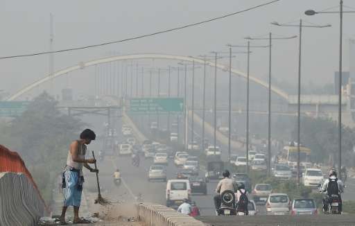 An Indian sweeper cleans a flyover as smog covers the New Delhi skyline