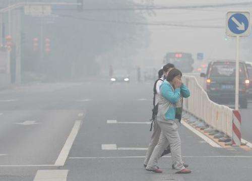 Pedestrians cover their faces as they cross a street in Beijing amid heavy smog on October 8, 2014